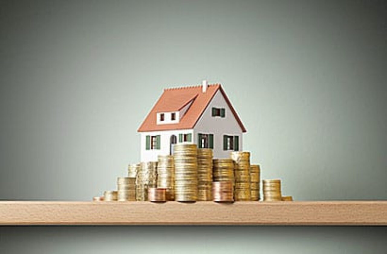 Miniature model house standing on a stack of coins.