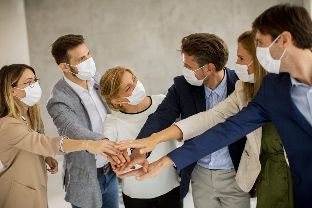 Group of business people with protective facial masks holding hands together in the office
