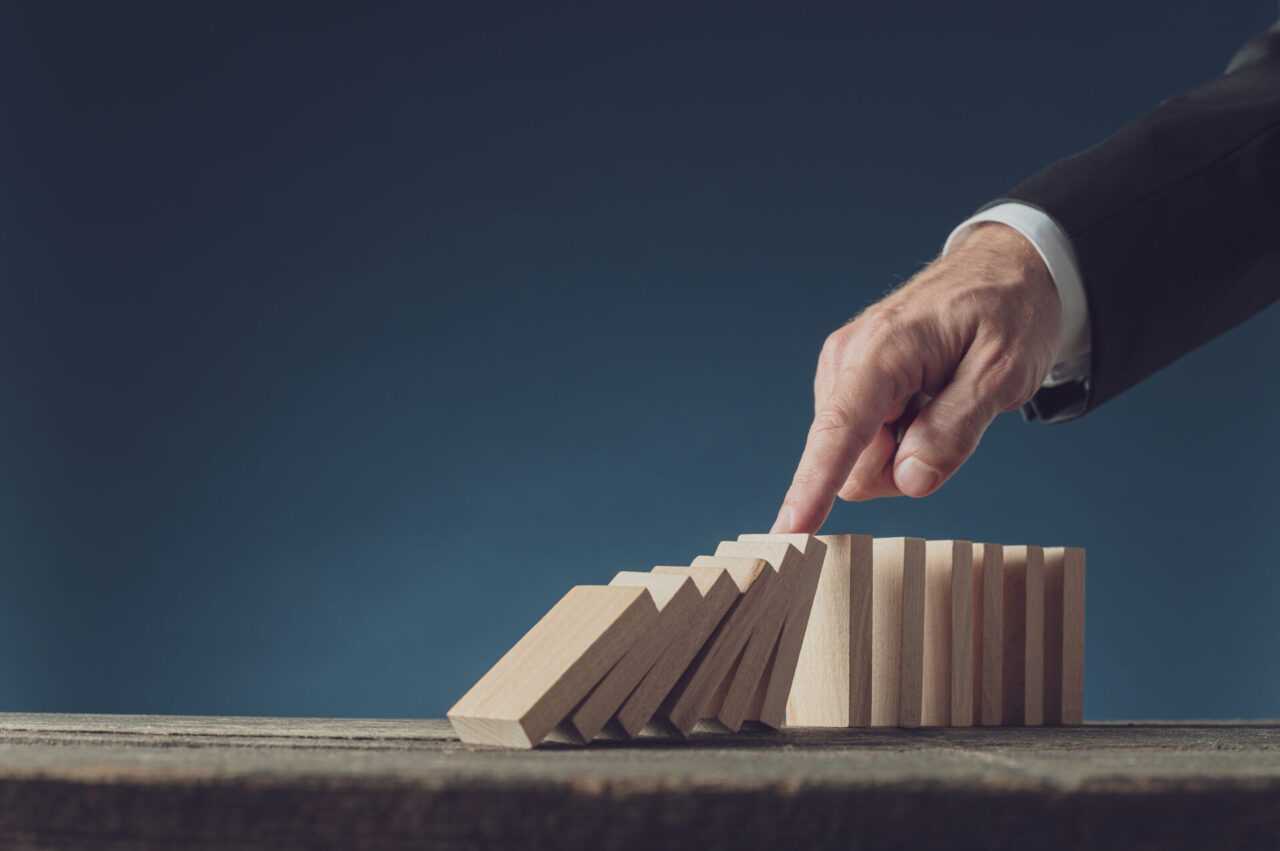 Business crisis manager stopping collapsing dominos with his finger. Over blue background with copy space.